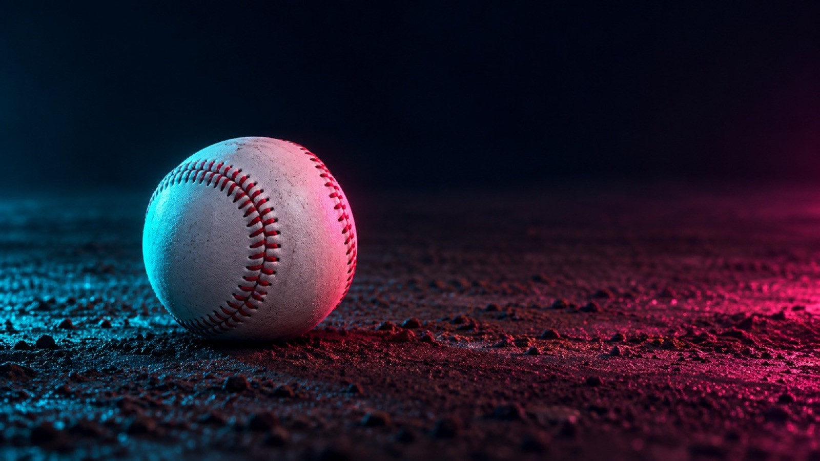 A plain baseball with red stitching rests on dark infield dirt.